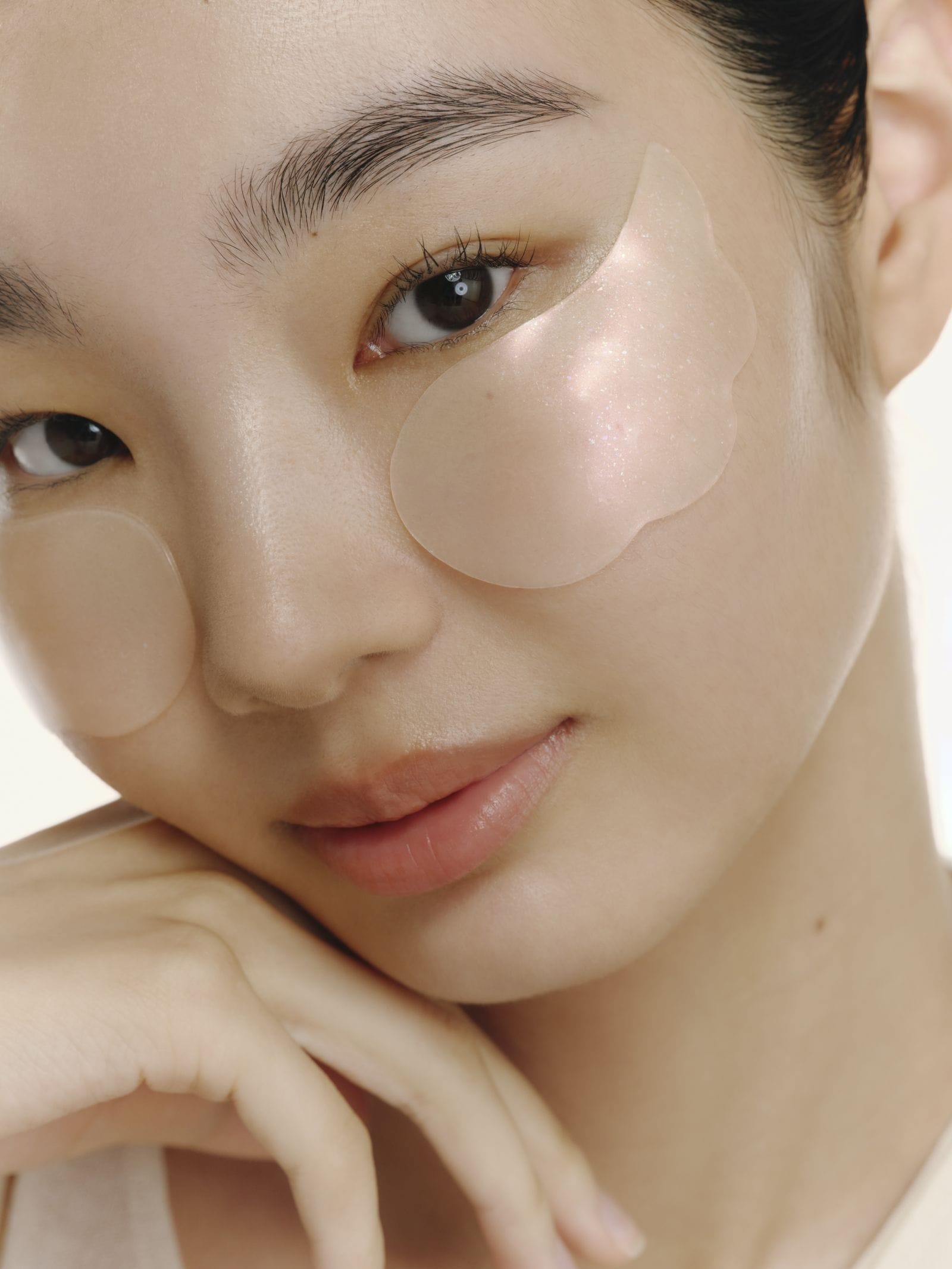 Close-up of a person wearing under-eye patches with a neutral background